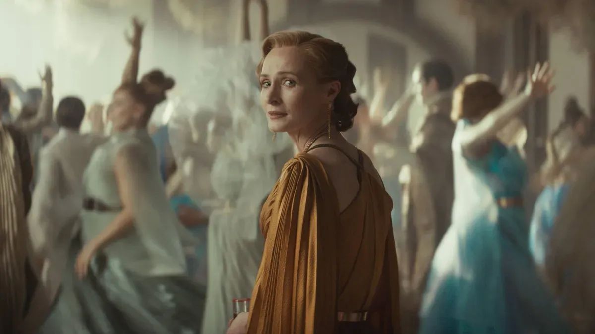 Mon Mothma, dressed in a golden dress, stands amid a group of revelers, dancing wildly. They are out of focus.