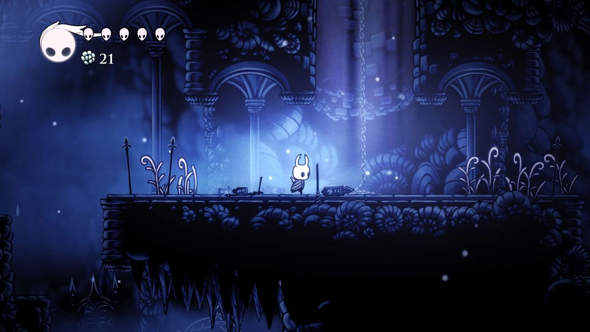A small creature in a white, horned helmet stands in a large, mostly blue video game level. It is empty but for them.