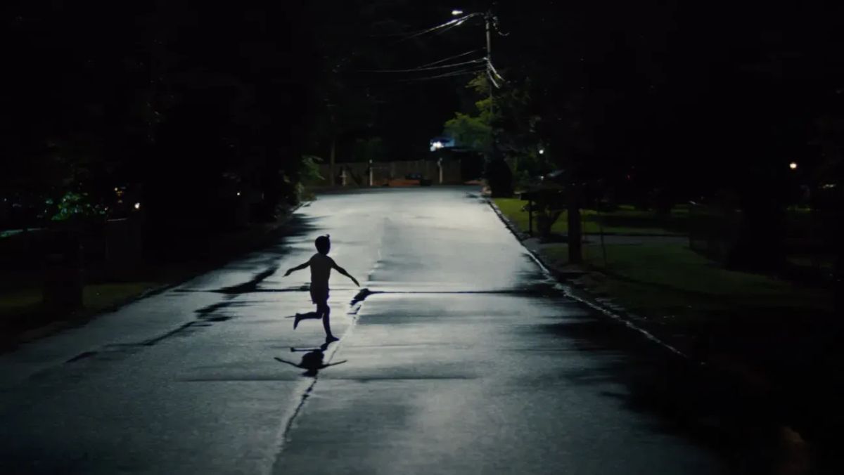 A child runs across a street in silhouette, their arms spread out wide to the side.