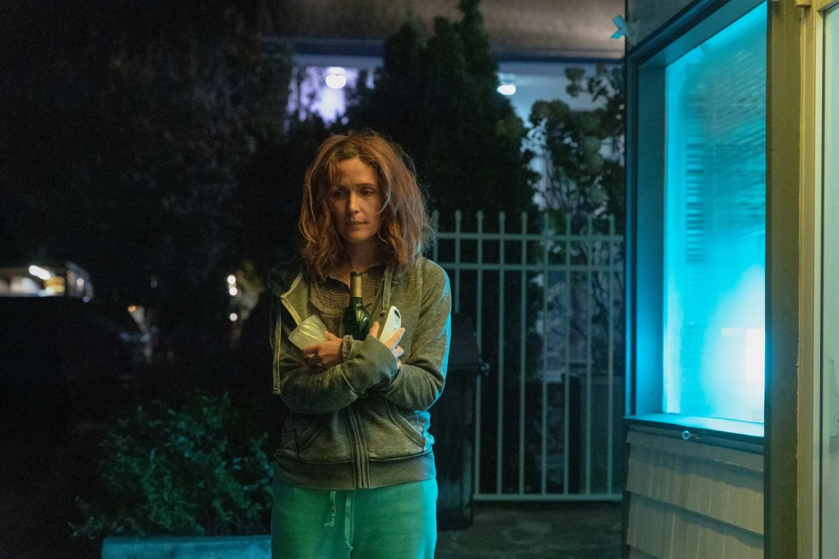 Rose Byrne, hair straggly and face glum, stands outside a hotel, clutching a bottle of wine and a baby monitor.