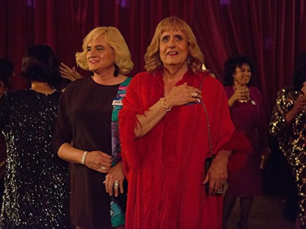 Marcie and Maura, dressed in vintage '90s fashion, enter a cross-dressing event with great joy.