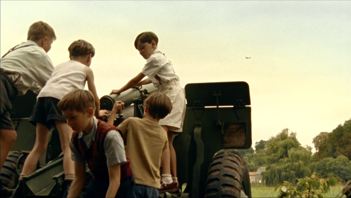 Boys clamber over a WWII-era tank while a plane flies overhead.