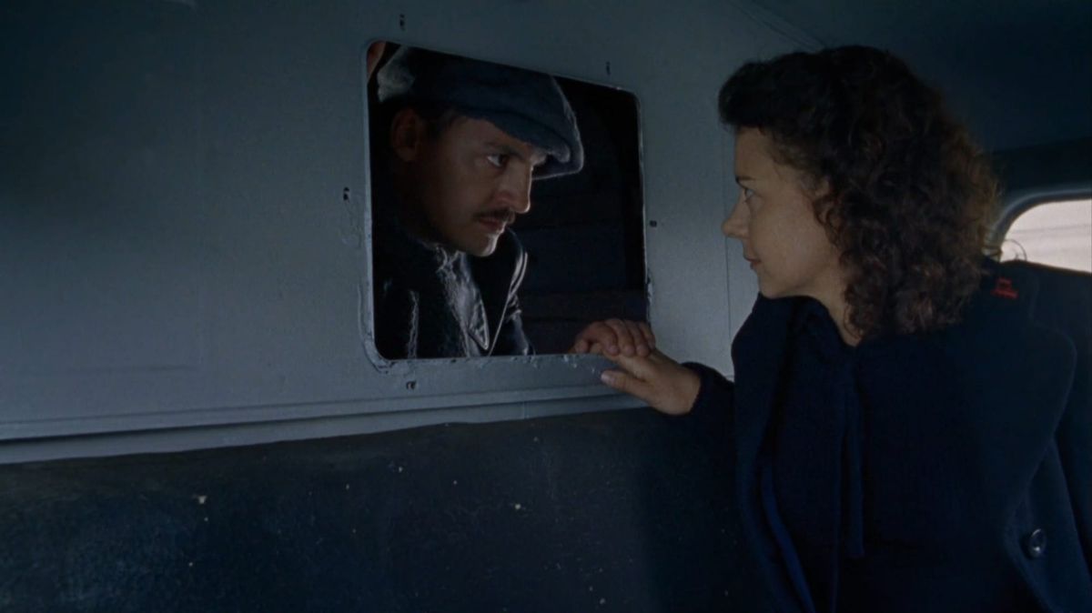 Marcel peeks through the little window into the back of Suzanne's mail truck, covering her hand with his.
