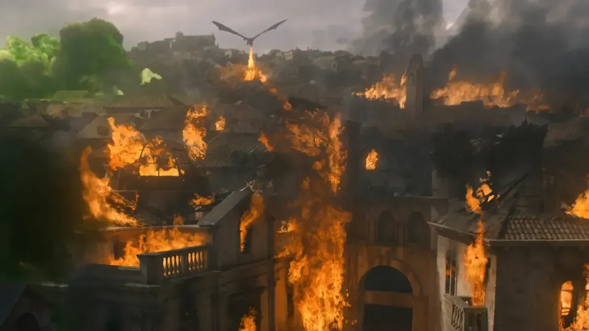 A dragon in shadow flies above a medieval city on fire. 