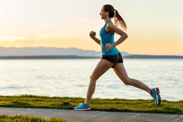 A woman in an aqua top, aqua shoes, and black running shorts runs alongside a river.