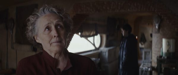 Maarva looks up to the ceiling tearfully as Cassian looks away in the background.