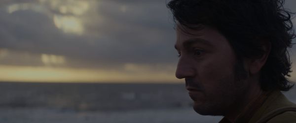 Cassian stares in a melancholy mood as the sun rises behind him. 