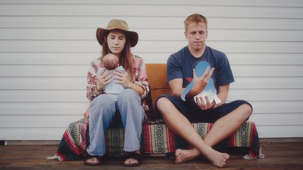 Two parents hold their babies. One of the babies is no longer present, replaced by blue sky.