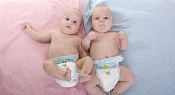 Two babies, both bald, both in diapers, lay on two blankets. One blanket is pink, the other blue.