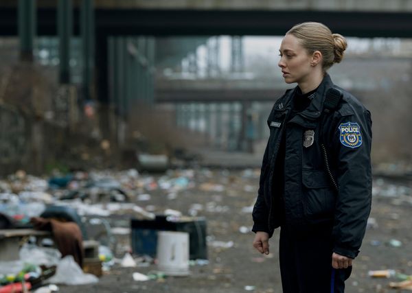 Amanda Seyfried in a Philadelphia police uniform stares with concern at a messy area covered in trash.