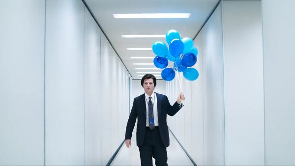 Mark S. (Adam Scott) is in a suit. He stands in a long, featureless, white hallway. He holds blue balloons with his face on them.