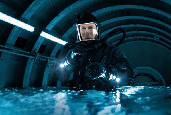 Tom Cruise in a dive suit in a cylindrical room, water roughly up to his waist. It's lit by fluorescents. It looks cold.