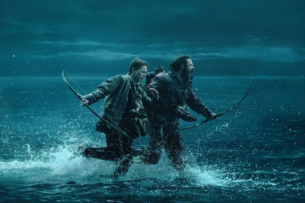 A boy and a man, both holding bows, crash through shin-deep water, running away from something. It's nighttime.