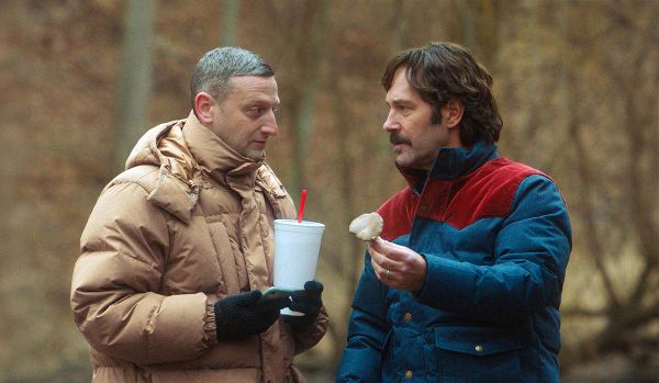 Tim Robinson, in a pure beige coat, clutching a huge soda cup, looks at Paul Rudd, in a colorful jacket. Rudd holds a mushroom.