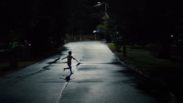A child runs across a street in silhouette, their arms spread out wide to the side.