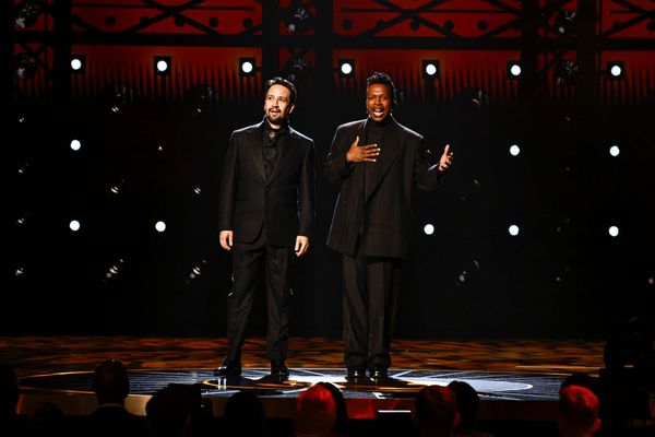 Lin-Manuel Miranda and Leslie Odom, Jr., both in all black suits, perform on a large stage.