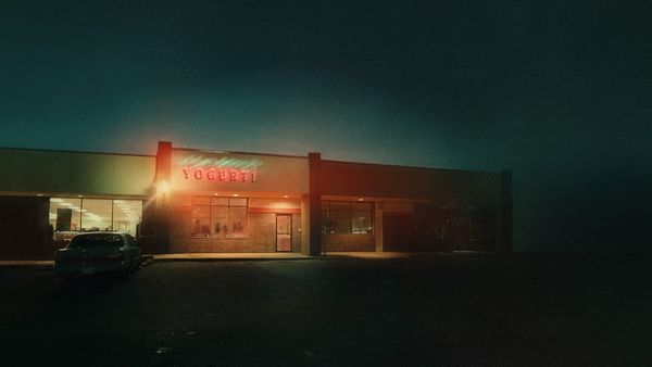In rather fuzzy, impressionistic key art, a yogurt shop is presented against a dark landscape. Its neon sign lights up the night.