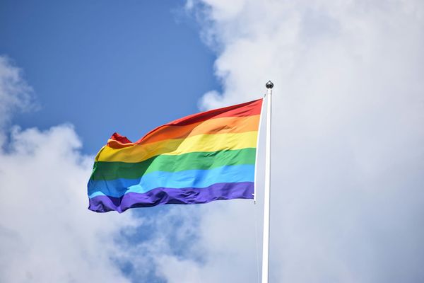 A rainbow Pride flag against a blue sky with white clouds.