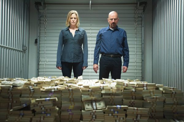 Skyler, a blonde woman in navy clothes, and Walter, a bald man in blue clothes, look at an enormous pile of money in a storage unit.