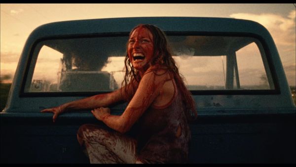 A woman, drenched in blood, laughs as she drives away from a threat in the back of a pickup.