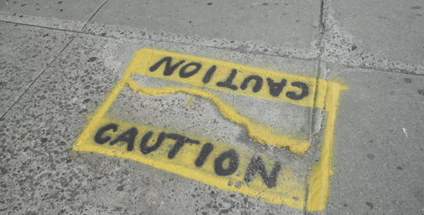 "Caution" written in spray paint around a broken section of concrete sidewalk