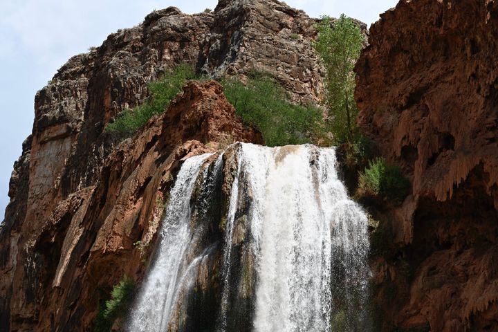 Close-up view of Havasu Falls, showing water flowing down rocky red cliffs, surrounded by desert vegetation.