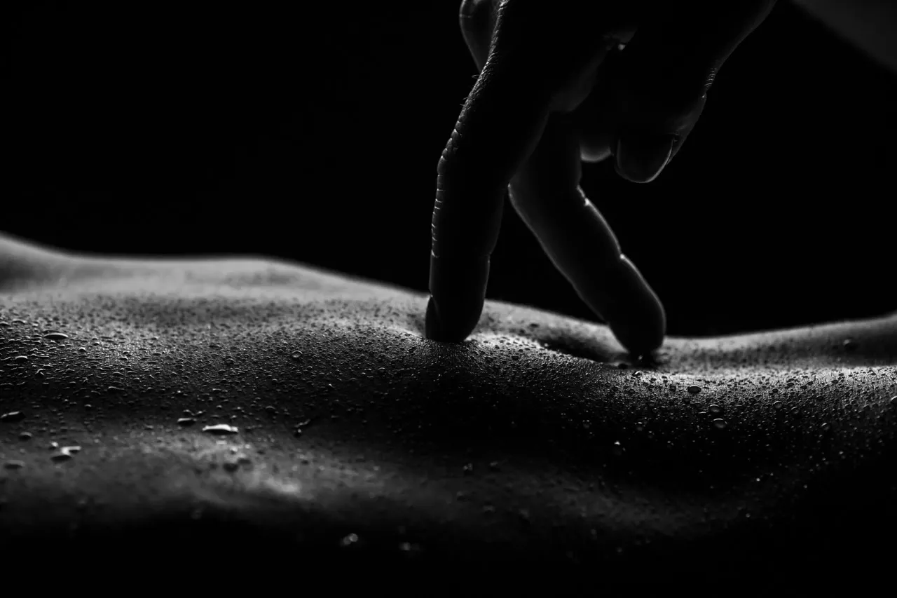 Wet look nude photography with hand touching textured body surface for mystery effect