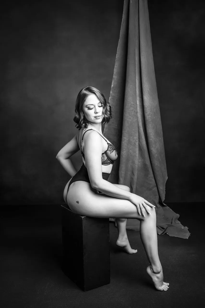Elegant lingerie pose on cube prop, photographed in small studio with textured fabric backdrop
