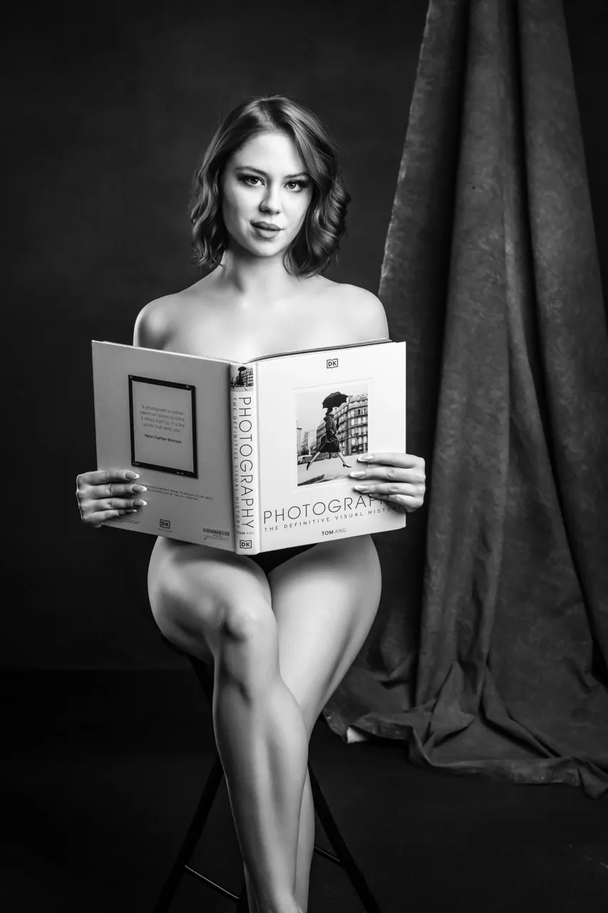 Tasteful boudoir image with a photography book prop, creating an artistic and editorial studio portrait