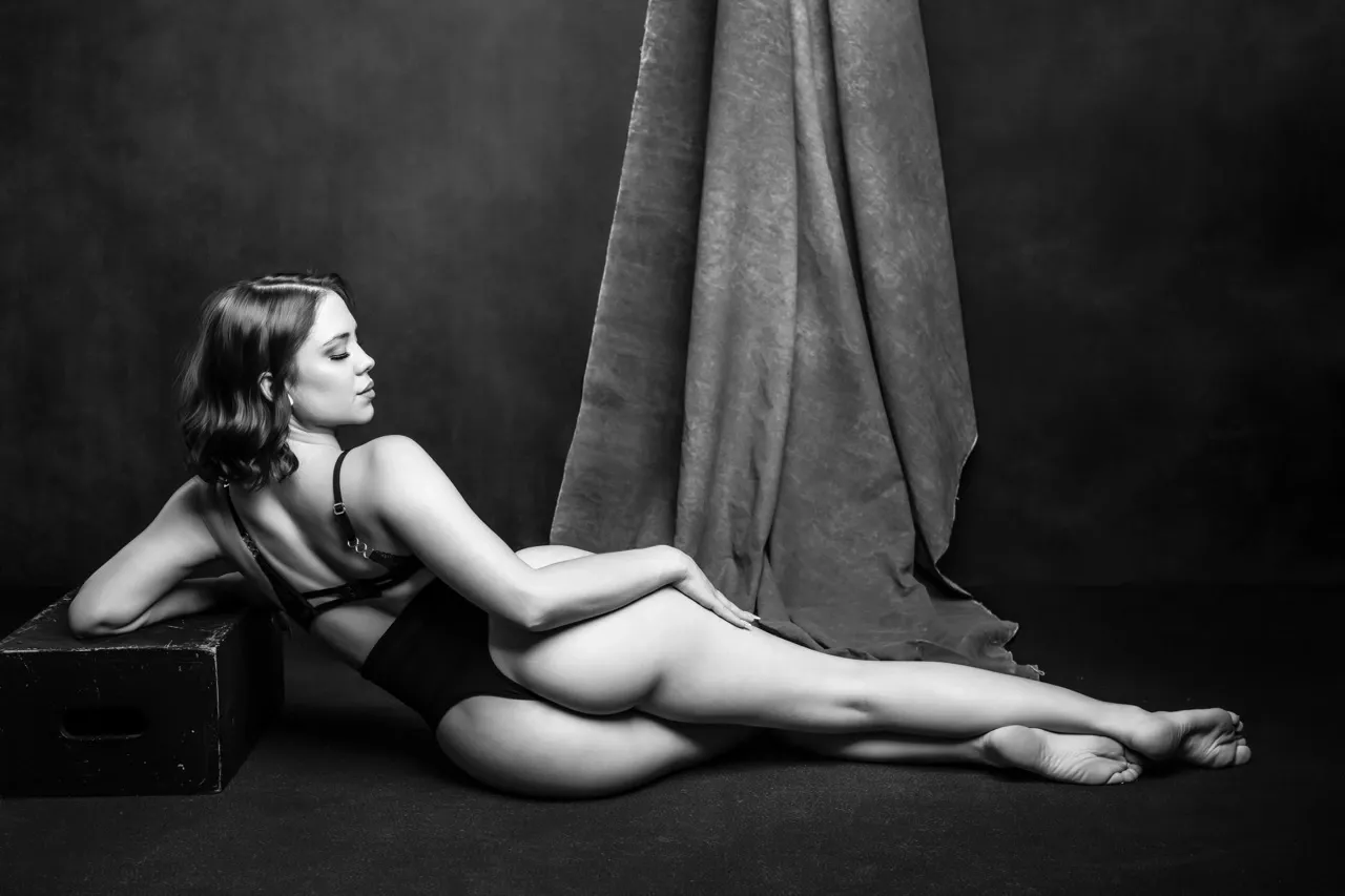Back view boudoir pose using fabric and a vintage cube prop for a soft editorial look in studio