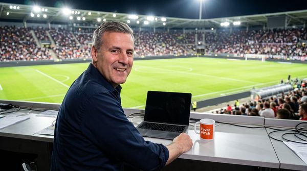 KI-Bild: Pit Gottschalk auf der Pressetribüne unter Flutlicht, neben dem Laptop die Fever-Pit'ch-Tasse