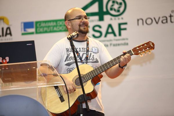 Eu, tocando violão, com um microfone em um pedestal e um laptop à frente.