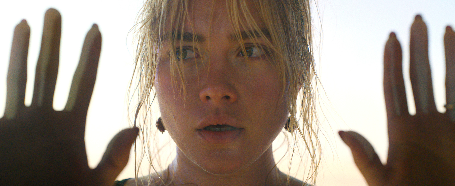 Film still from DON'T WORRY DARLING featuring Florence Pugh with her hands up, touching the screen.