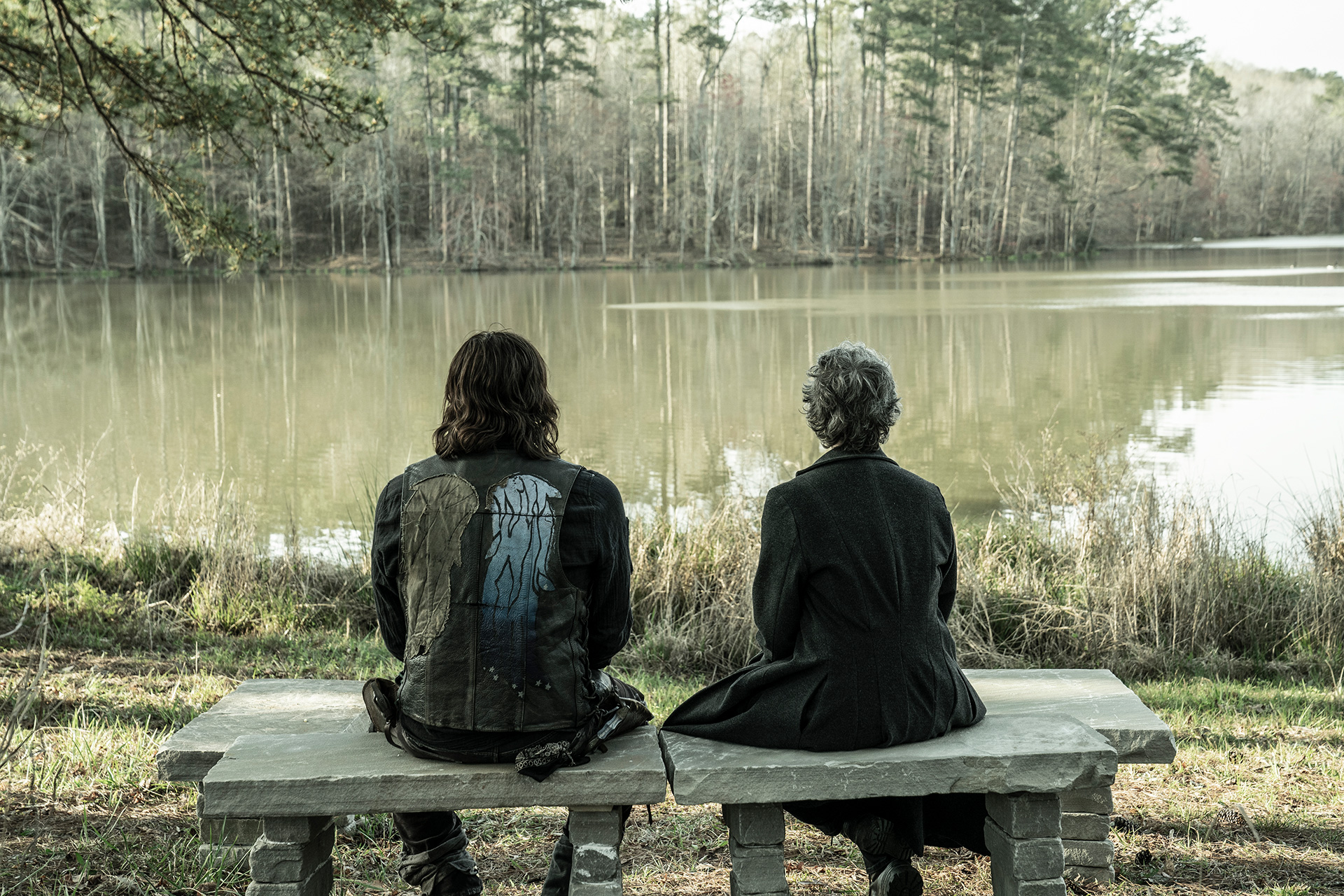 THE WALKIN DEAD still with Norman Reedus and Melissa McBride sitting on a bench, looking out at a lake with backs to us.
