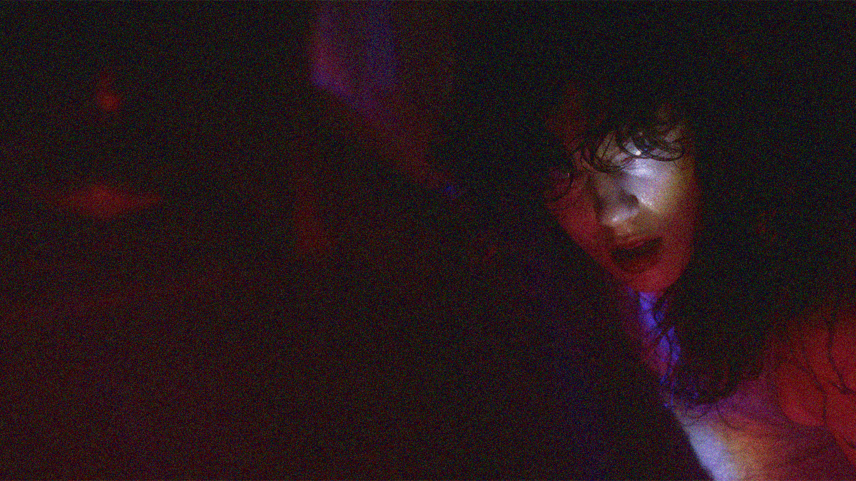 A woman far right light so only her face is visible against the darkness.