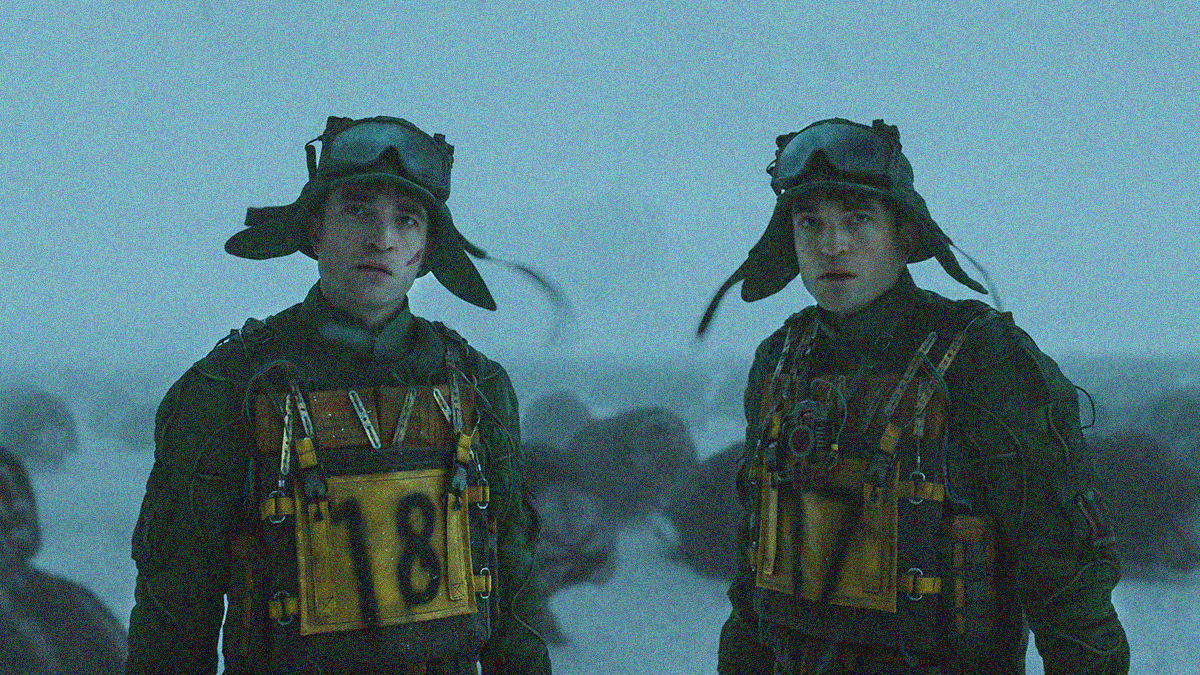 Two Robert Pattinsons strapped with explosives looked towards the camera while standing in a blizzard with alien creatures roaming behind them.