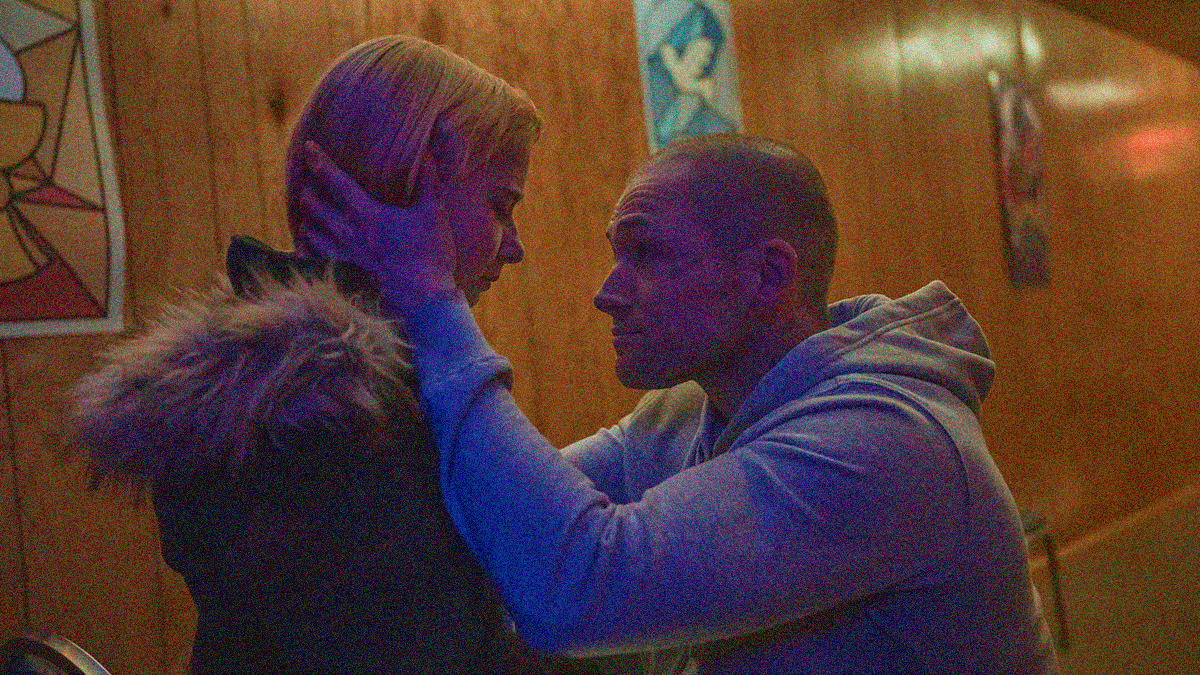 A man crouches and holds his daughter's head in his hands.