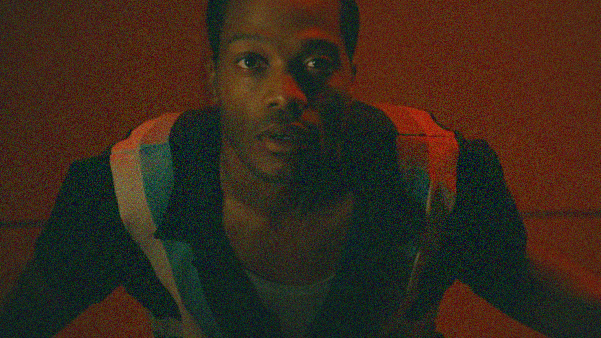 A man looks up to the sky under a red glow with arms stretching out to his sides.