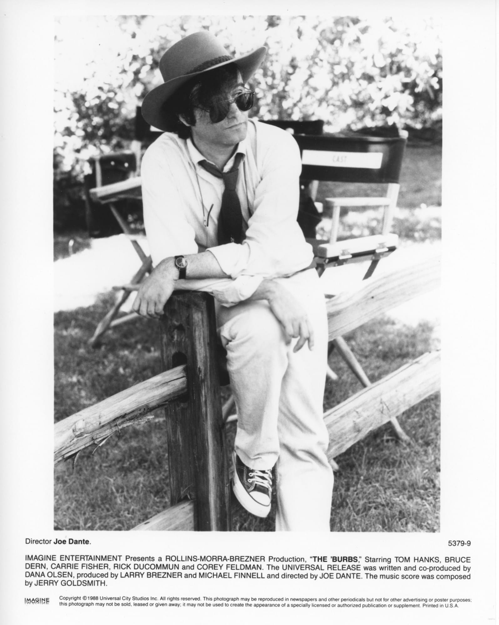 THE 'BURBS director Joe Dante - shown sitting/leaning on a wooden fence post with set chairs behind him. 