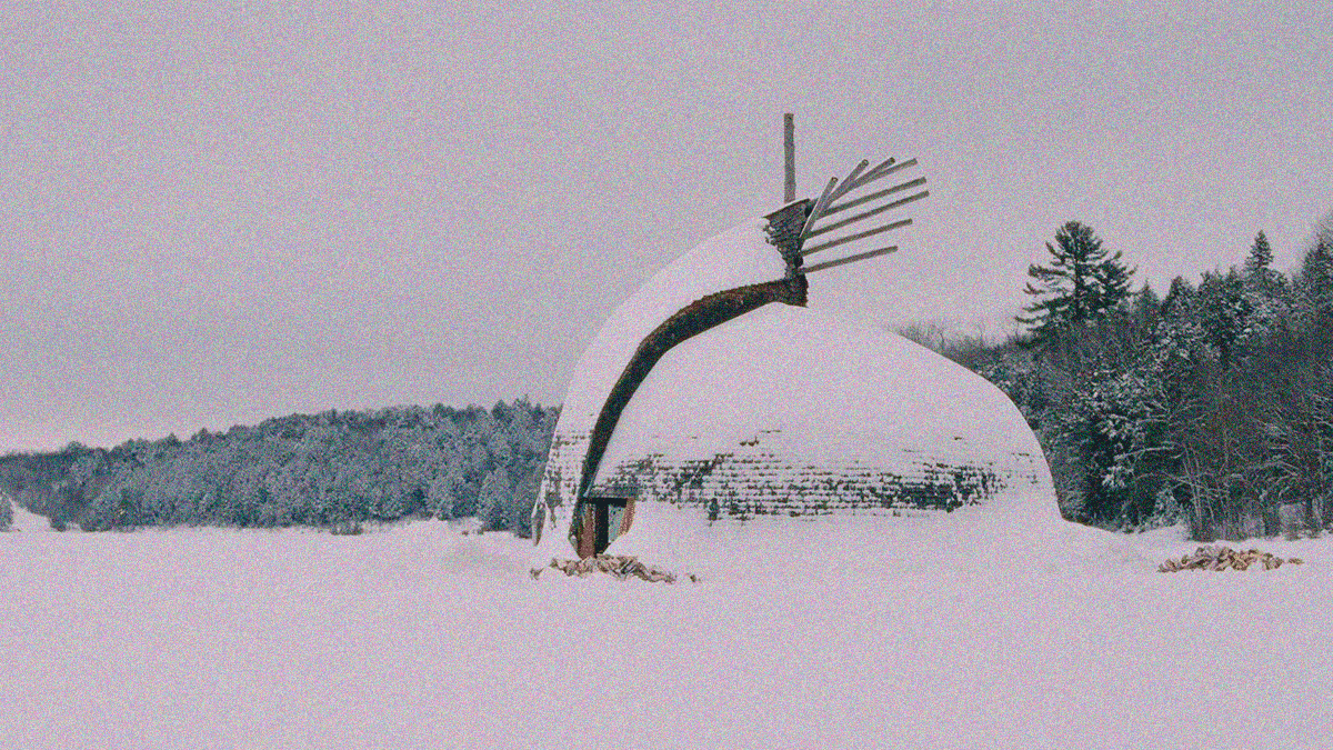 A snow-covered dome-shaped structure against a backdrop of forest.