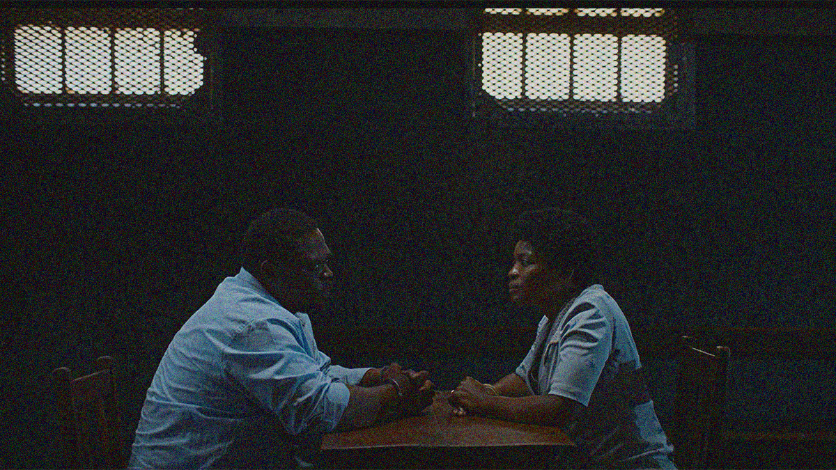 A man and woman sit across from each other at a small table. He is in handcuffs.