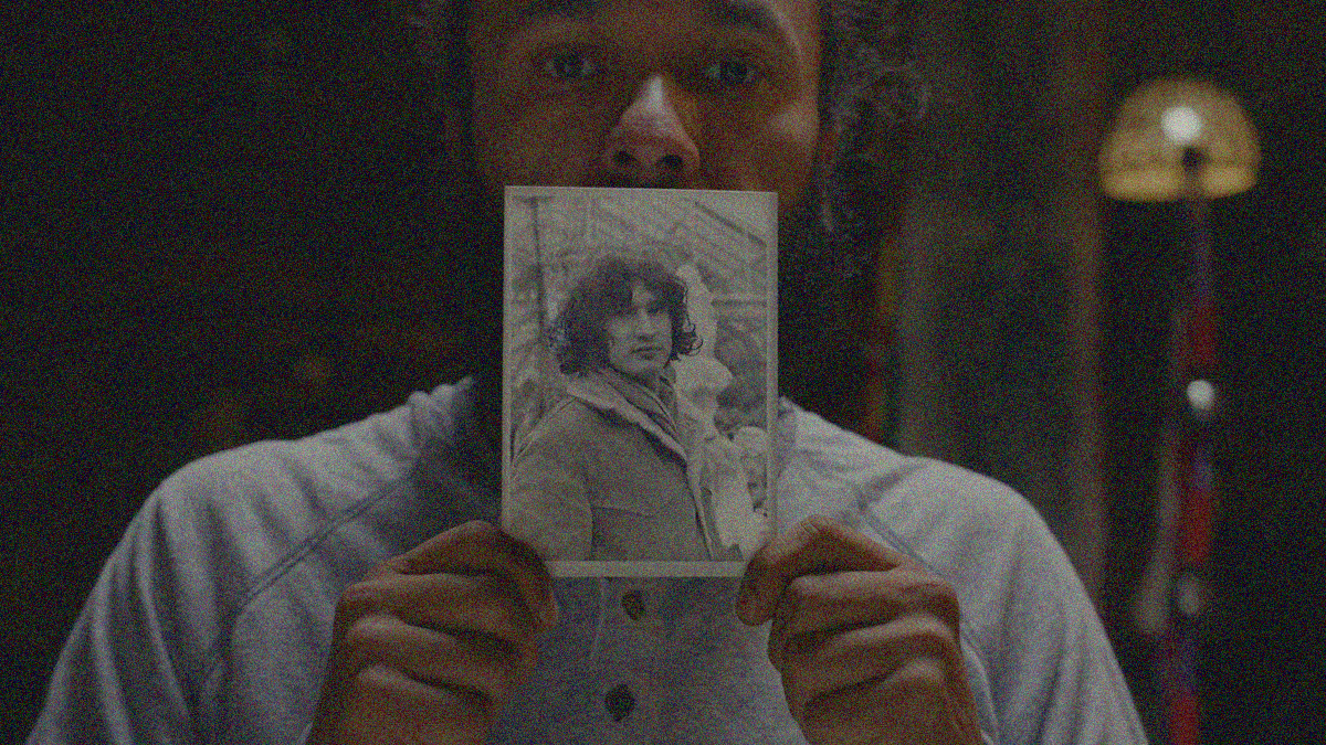 A man holds up a photograph of another man.