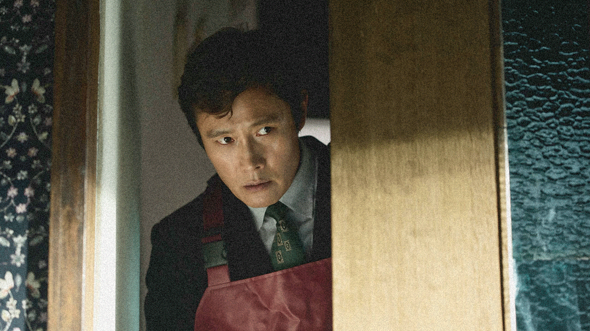 A man in rubber overalls peers cautiously around the edge of a partially closed door.