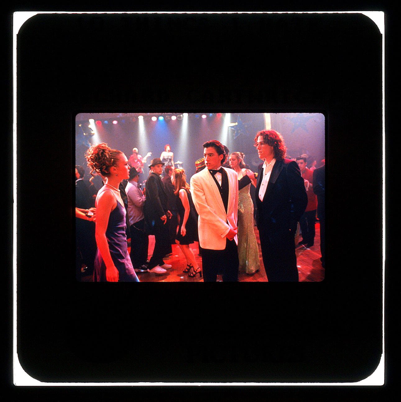 A woman (left) and man (right)—prom dates at the dance—are separated by a second man in white tuxedo.