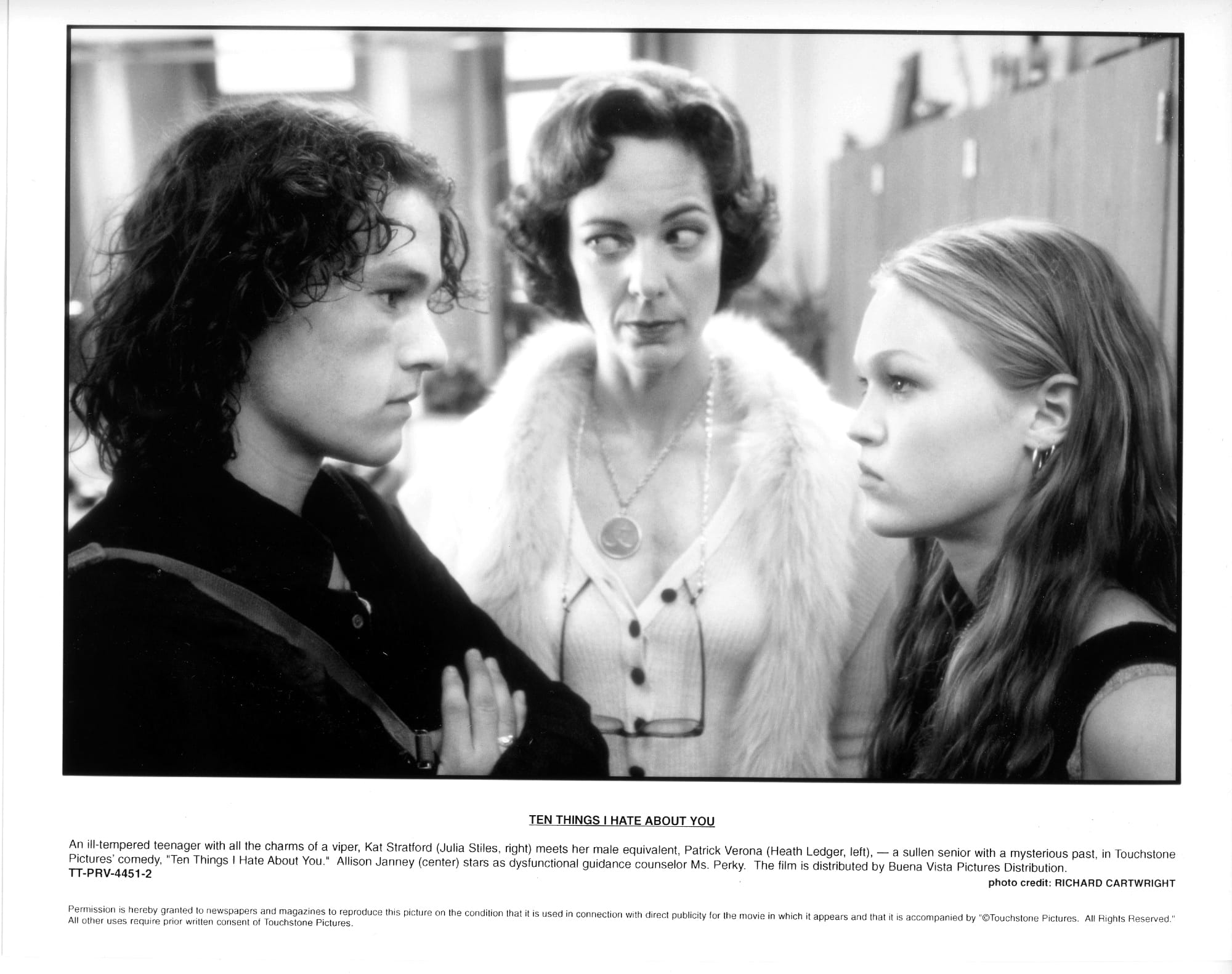 A woman with glasses hanging on a chain around her neck stands between a high school boy and girl scowling at each other.