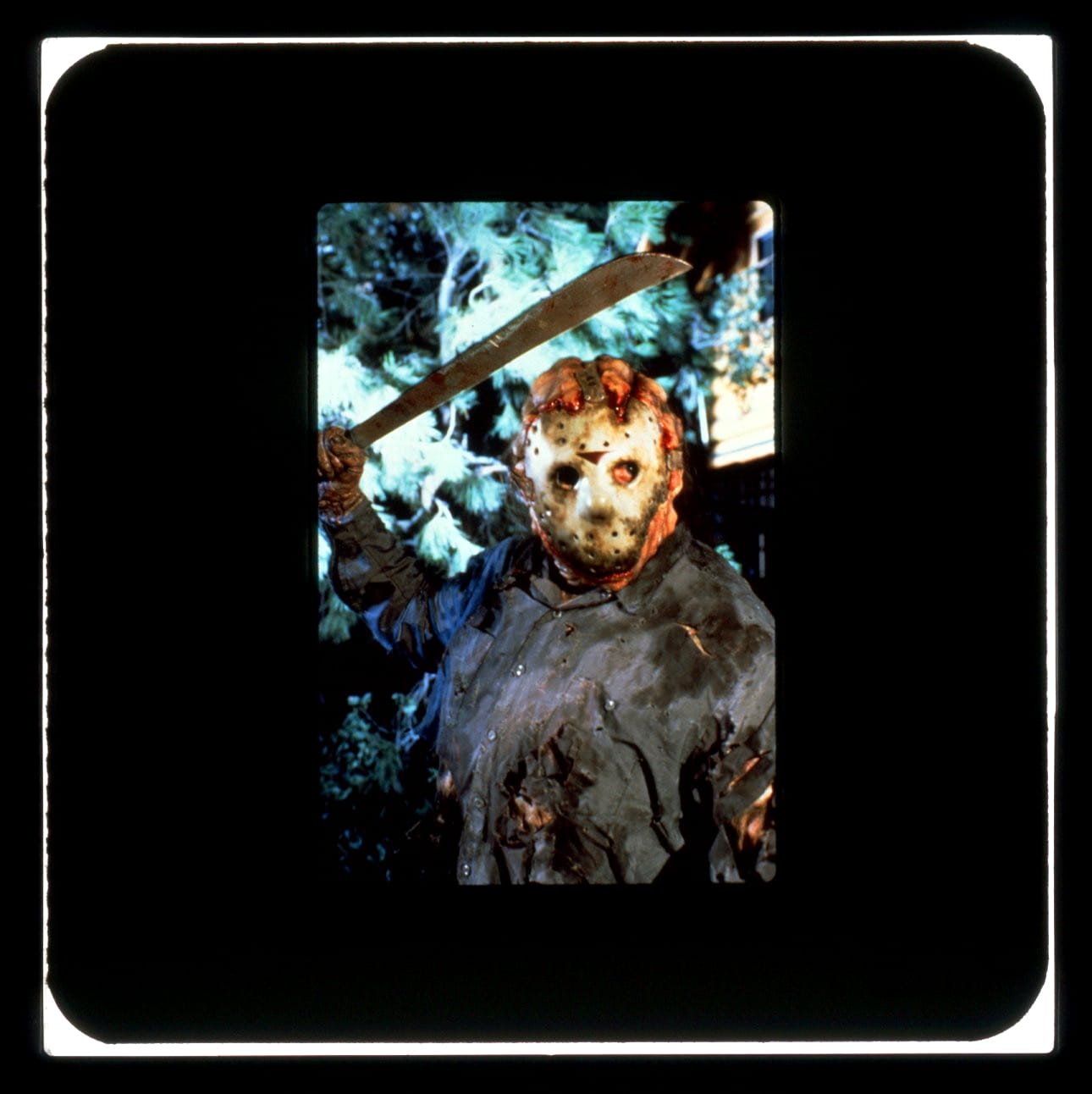 A battered and charred Jason Voorhees in goalie mask looks at camera with machete raised.