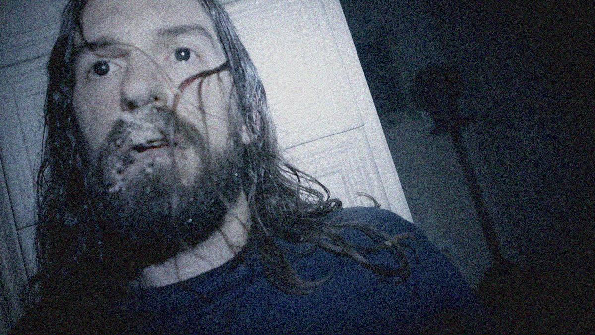 Close-up of a man with long hair and beard seemingly hiding behind a white dresser, a white substance is in his mustache.