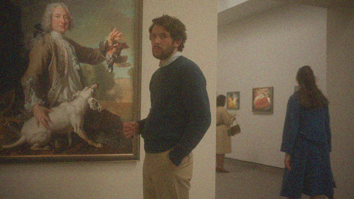 A man looks towards the camera while standing in front of a painting hung inside a public gallery.