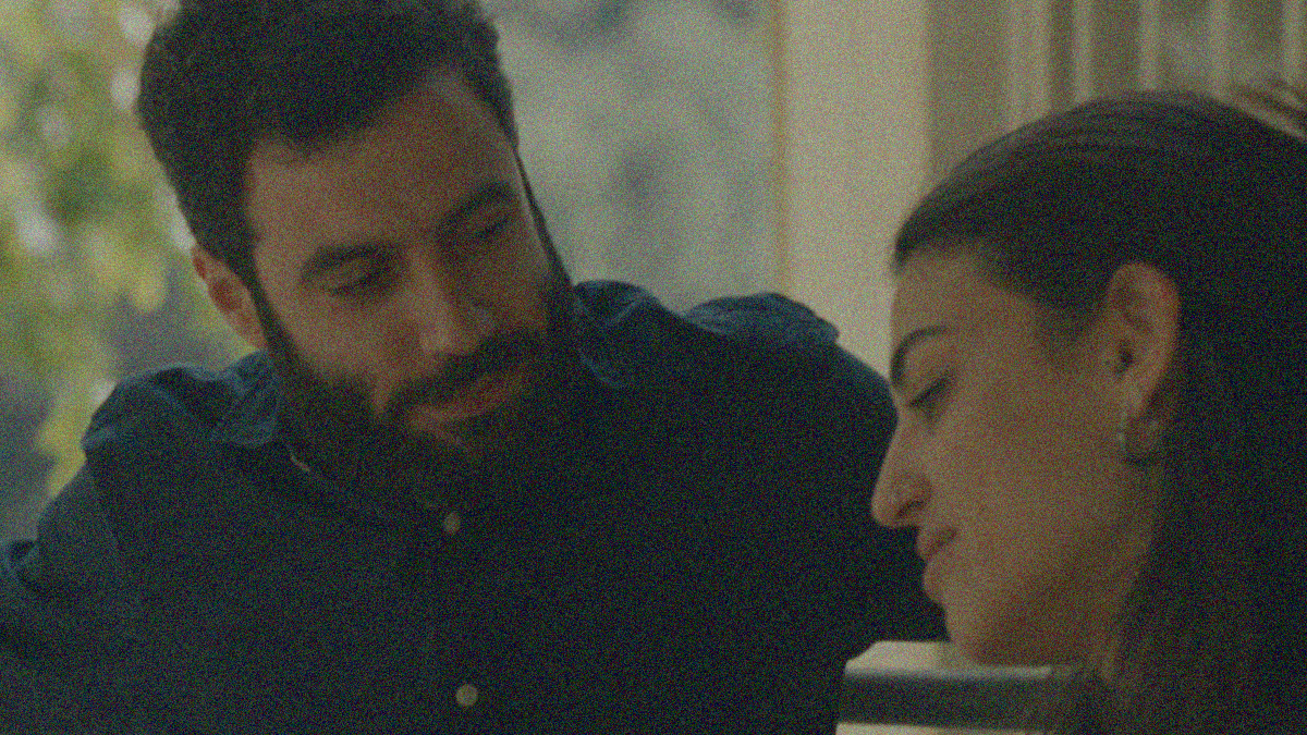 A bearded man in a button-down looks down with a smile at a woman looking downward.