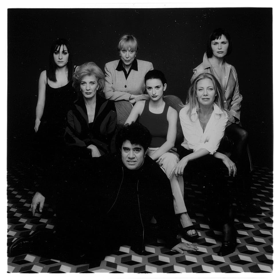Posed cast photo with three woman in the back row, three sitting in the center, and the director lounging on the floor in front of them all.
